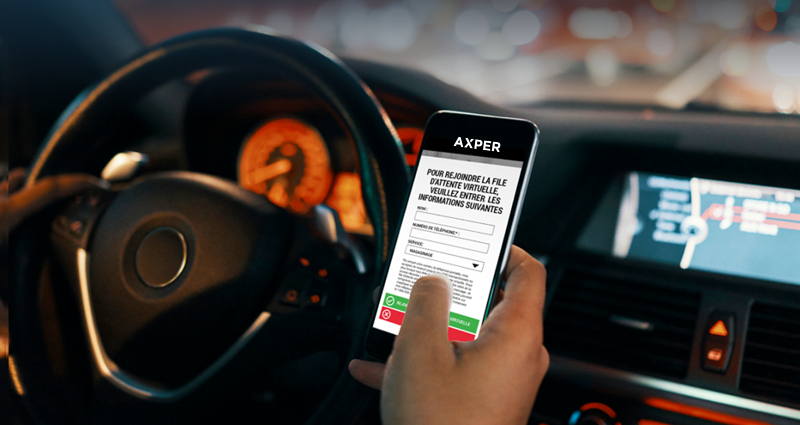 Version mobile de l'image d'un téléphone dans une voiture, affichant l'application de file d'attente d'Axper. L'écran affiche "Pour rejoindre la file d'attente virtuelle, veuillez entrer les informations suivantes".